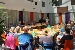 Een grote groep mensen in een zaal, aan tafel in theater opstelling, kijkend naar een presentatie